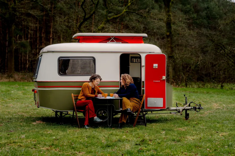 Niki en Ester drinken koffie voor de caravan
