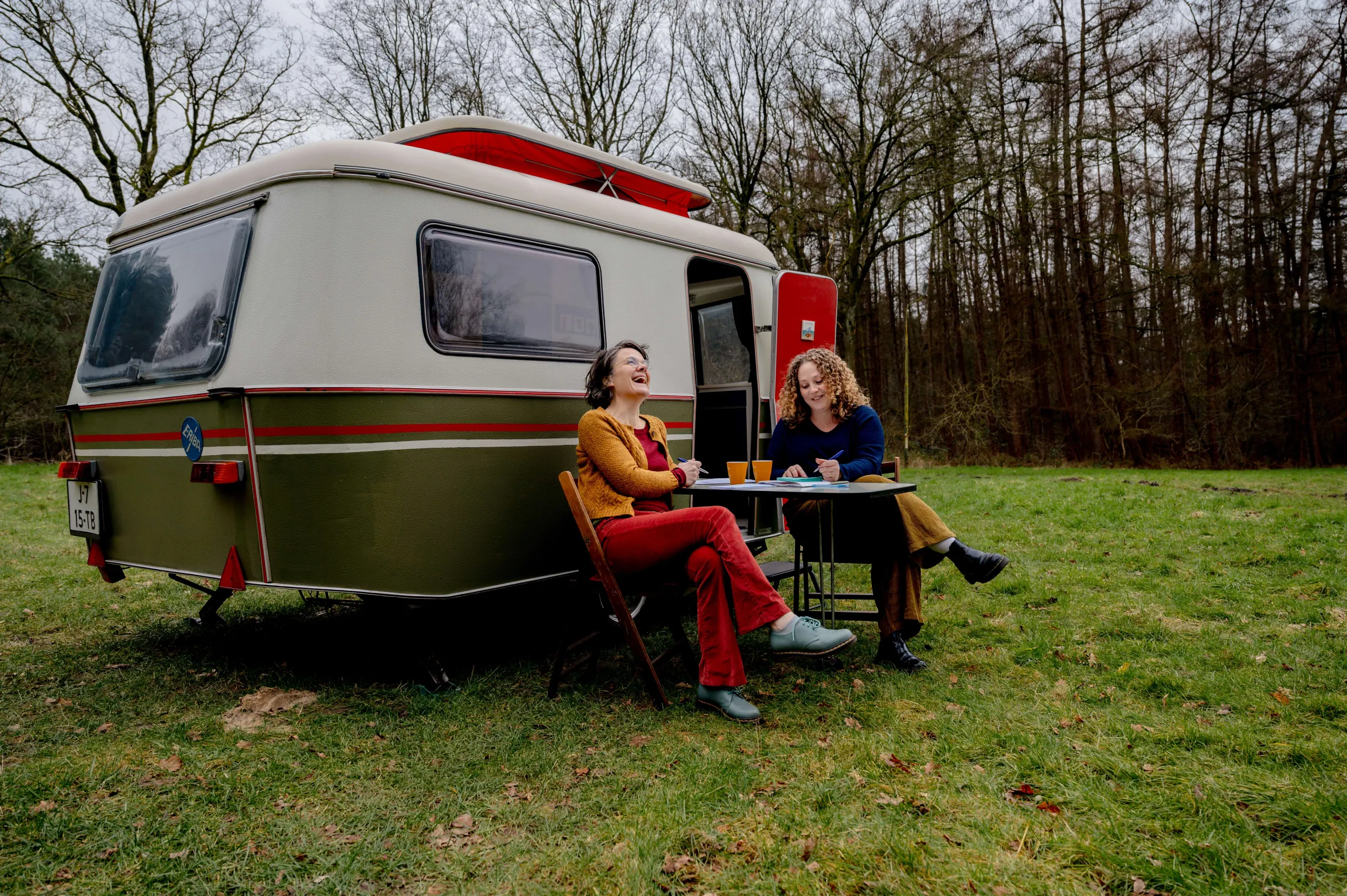 Ester en Niki zitten lachend voor hun caravan